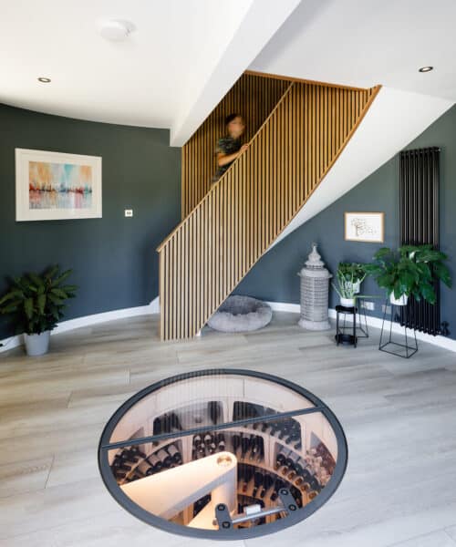 Entrance hall showing the glass topped underground wine vault and wood panelled stairway at Whitsunden Oast, a contemporary extension & barn conversion designed by Hawkes Architecture.